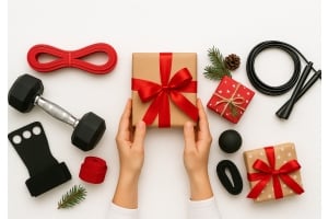 Ett brunt paket med rött sidenband som två händer håller i. En hexhantel, hand grips, hopprep och gummiband ligger runt om.