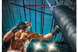 Ung vältränad boxare i shorts boxar på en svart boxningssäck