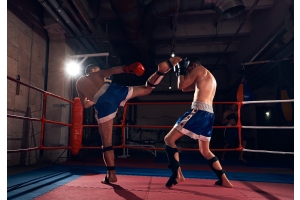 Två män i blå shorts och benskydd tränar kickboxning på en boxningsklubb