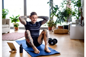 En ung tatuerad man tränar och gör situps i sitt vardagsrum