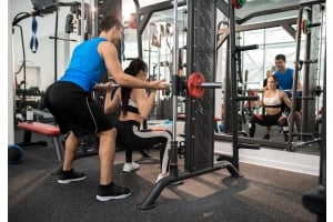 En personlig tränare hjälper en ung kvinna att göra benböj i en smithmaskin på ett gym