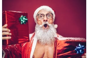 En vältränad äldre tomte håller i två julklappar och ser förvånad ut