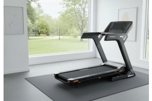 Ett löpband från Nordic Fighter i ett hemmagym med stora fönster och grönskande trädgård på utsidan.