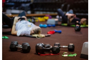Ett grupppass med styrketräning i bakgrunden, synliga hantlar och gummiband längst fram. 