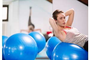 En ung kvinna gör situps på en blå pilatesboll